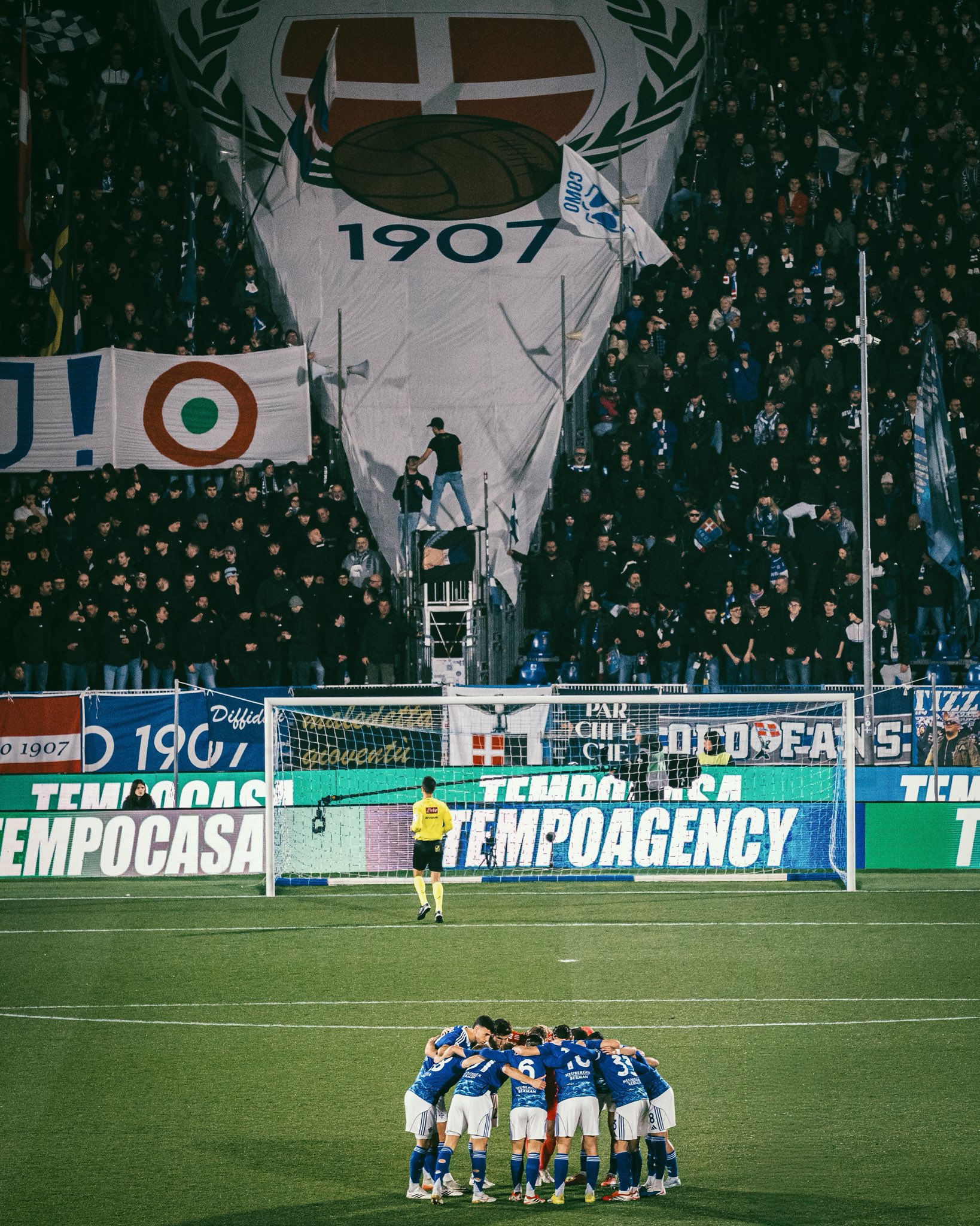 Como 1907 pre-match huddle with the Curva Norte tifo behind them